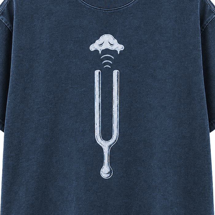 Detail crop of the Odd Habit Low Frequency slate-blue tee digital mockup, showing a tuning fork, sound waves and cloud. Not a production-sample photograph.